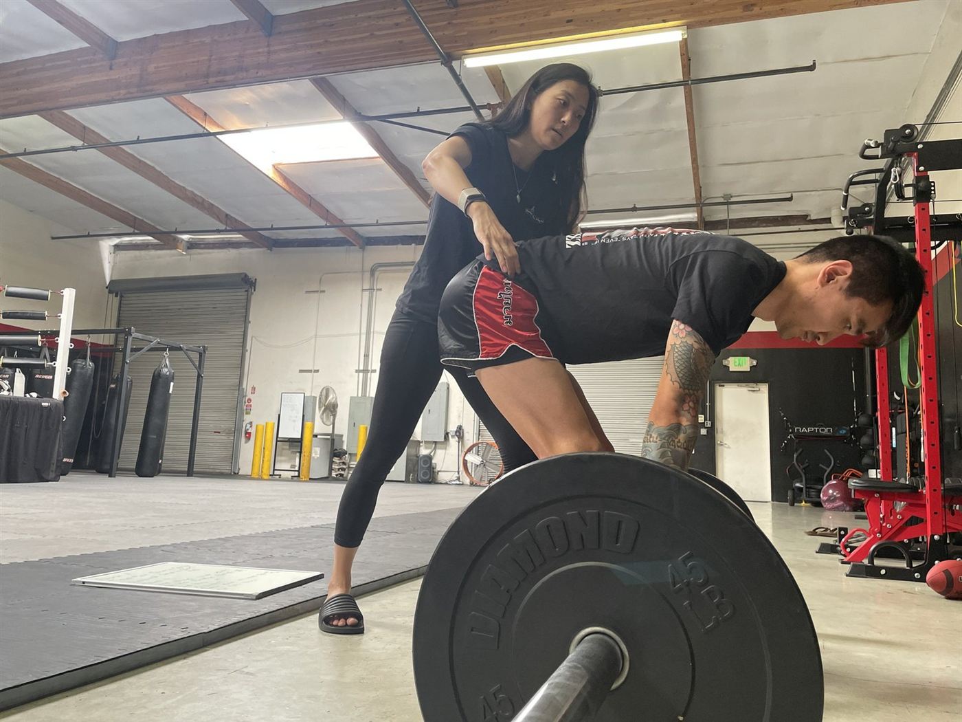 Dr. Lorrain Ko guiding a client's hip hinge as he sets up a barbell deadlift in the gym