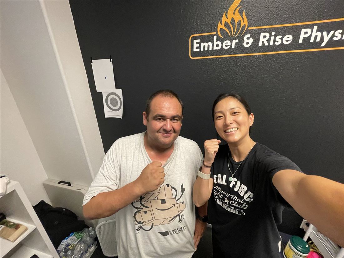 Dr. Ko and a client raising their fists in front of the Ember & Rise Physio sign