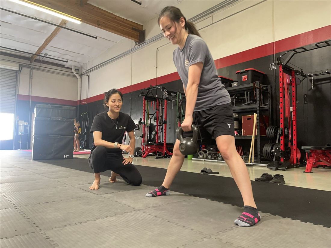 Dr. Ko kneeling to watch a client's form during a kettlebell lift