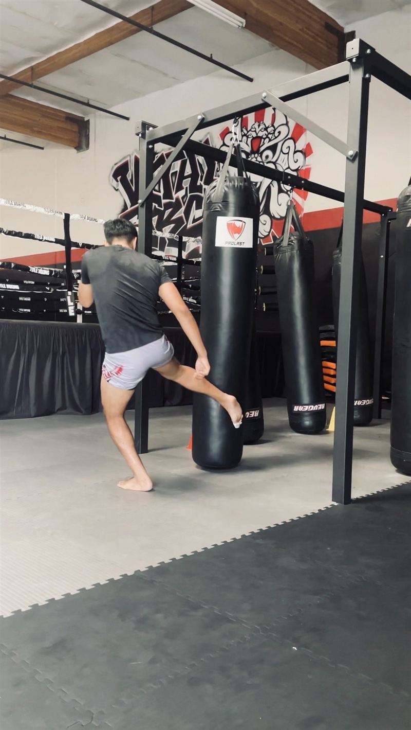 A client throwing a kick at a heavy bag in the Muay Thai gym